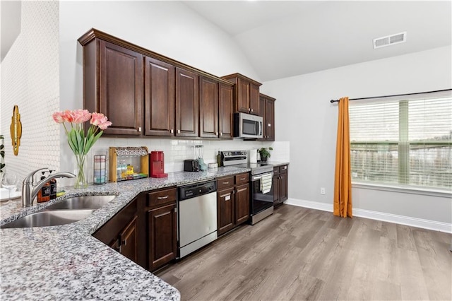 kitchen with stainless steel appliances, light stone countertops, sink, light hardwood / wood-style floors, and lofted ceiling