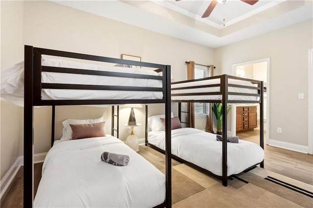 bedroom with ensuite bathroom, ceiling fan, a raised ceiling, and light hardwood / wood-style flooring