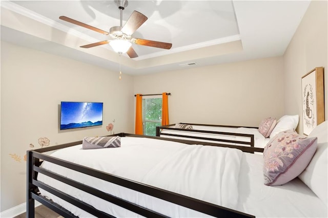 bedroom with hardwood / wood-style flooring, ceiling fan, and a raised ceiling