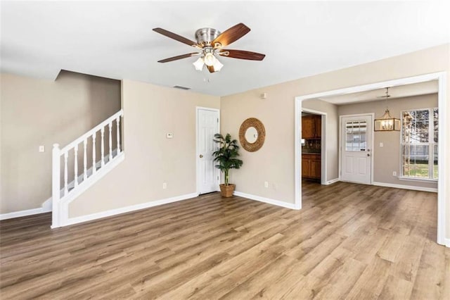 empty room featuring baseboards, visible vents, stairway, light wood-type flooring, and ceiling fan with notable chandelier