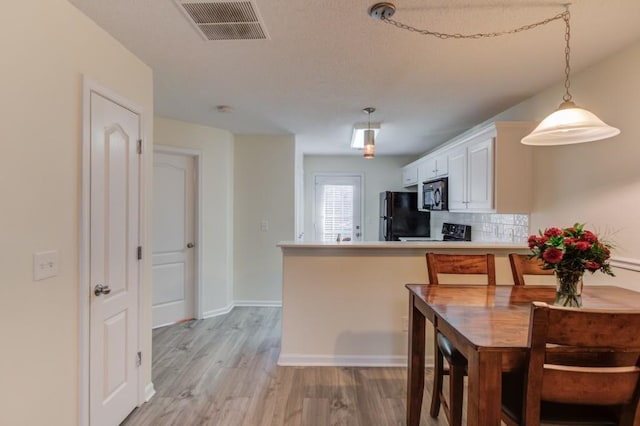 kitchen featuring light wood-type flooring, visible vents, black appliances, backsplash, and white cabinetry