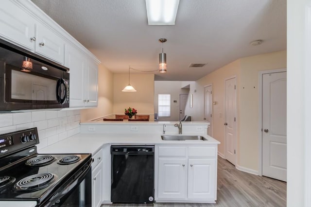 kitchen with light wood finished floors, a peninsula, a sink, black appliances, and white cabinetry