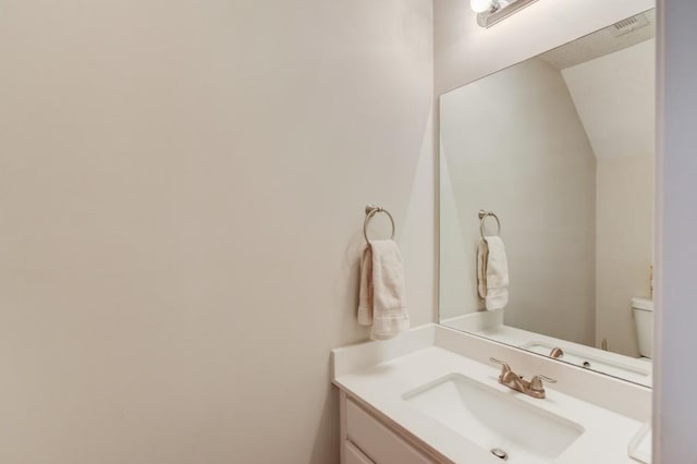 bathroom featuring lofted ceiling, toilet, and vanity