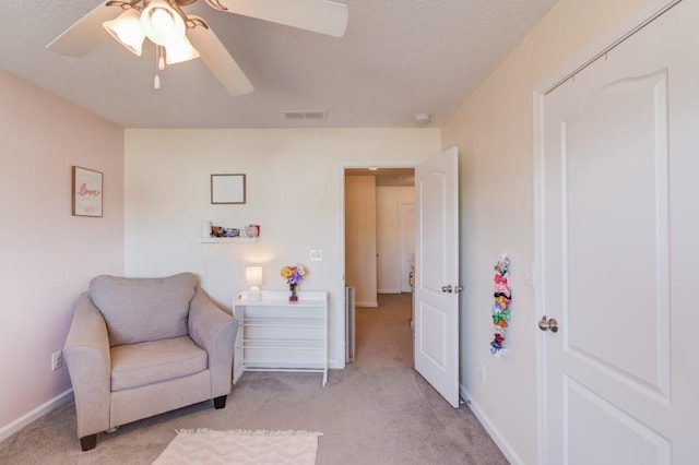 sitting room with visible vents, light carpet, a textured ceiling, baseboards, and ceiling fan
