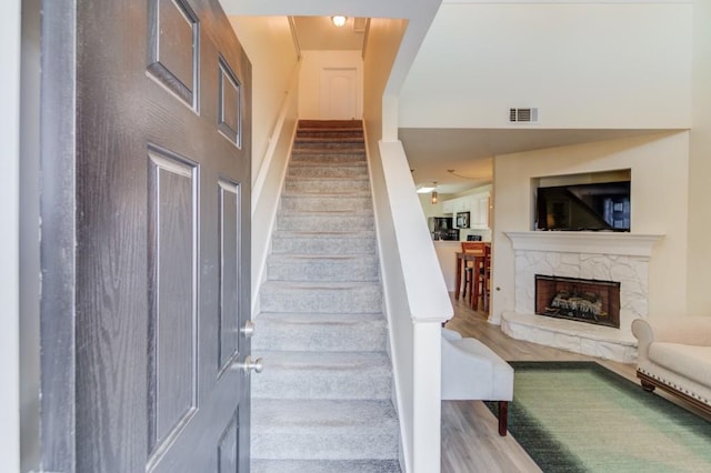 staircase with visible vents, a stone fireplace, and wood finished floors