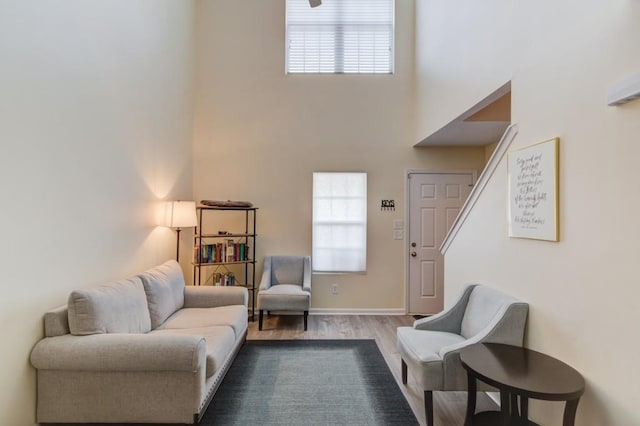 living area featuring a healthy amount of sunlight, a high ceiling, baseboards, and wood finished floors