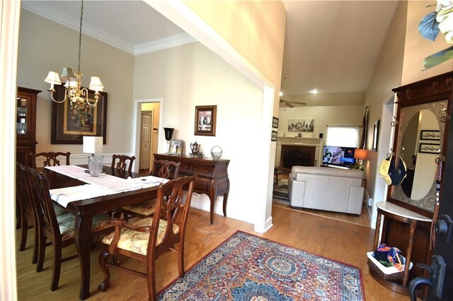 dining space featuring hardwood / wood-style floors, ceiling fan with notable chandelier, high vaulted ceiling, and crown molding