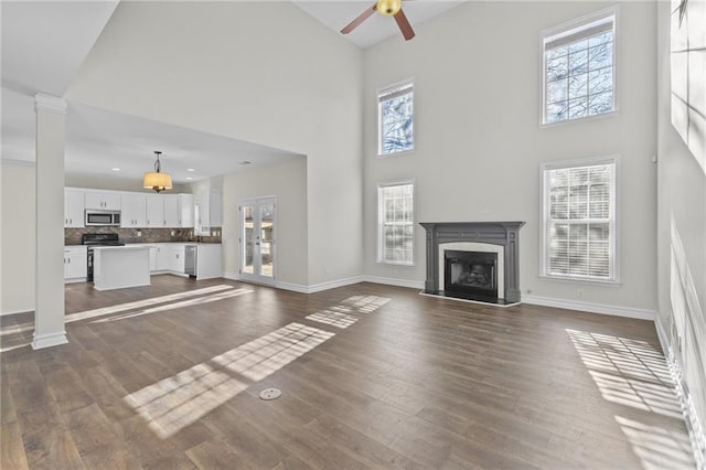 unfurnished living room featuring baseboards, a fireplace, a high ceiling, dark wood-style floors, and a ceiling fan