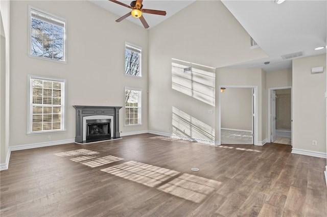 unfurnished living room with wood finished floors, baseboards, a fireplace, ceiling fan, and a towering ceiling