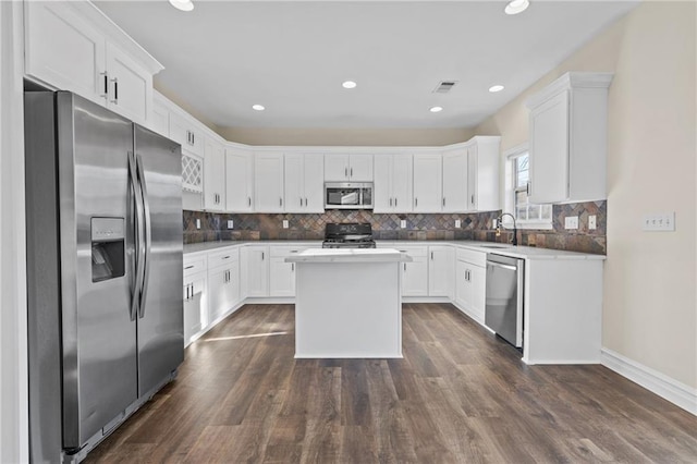 kitchen with a sink, stainless steel appliances, decorative backsplash, and white cabinetry