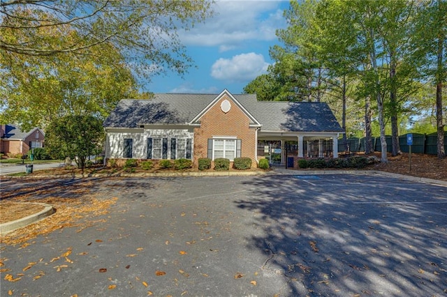 view of front of house with brick siding, uncovered parking, and fence