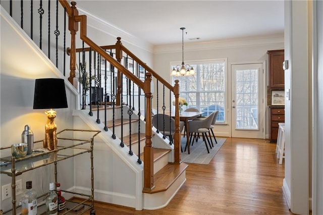 staircase with an inviting chandelier, crown molding, baseboards, and wood finished floors