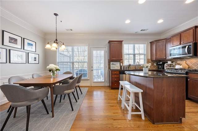 kitchen featuring light wood finished floors, visible vents, a kitchen island, stainless steel microwave, and ornamental molding