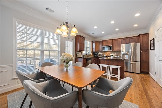 dining room featuring visible vents, crown molding, light wood-style flooring, and an inviting chandelier