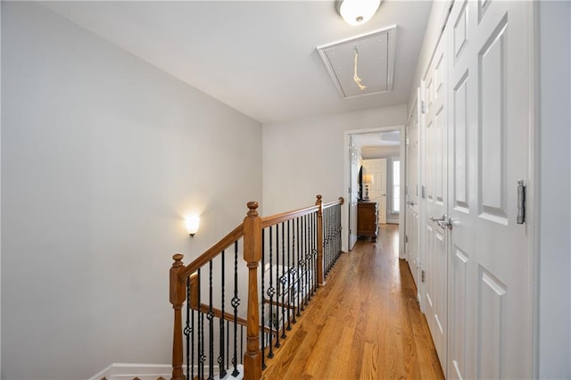 corridor featuring light wood-style flooring, an upstairs landing, and attic access