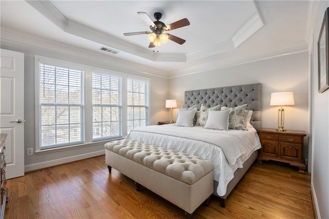 bedroom with visible vents, baseboards, light wood-style floors, a tray ceiling, and crown molding