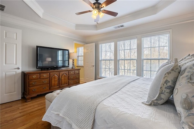 bedroom with a tray ceiling, wood finished floors, visible vents, and crown molding