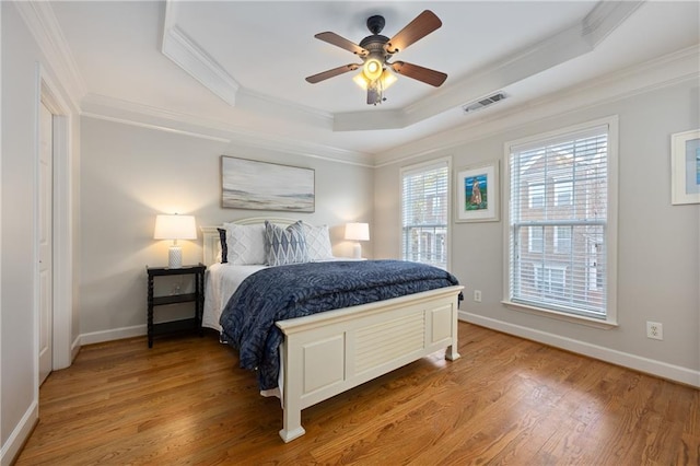 bedroom featuring a raised ceiling, visible vents, crown molding, and wood finished floors