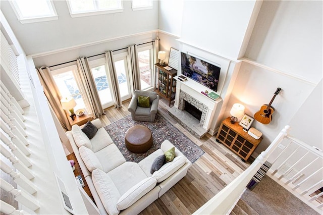 living area with a fireplace with raised hearth, wood finished floors, and a towering ceiling