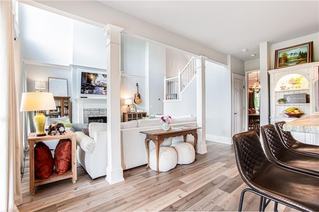 living area featuring light wood-style flooring, a stone fireplace, stairs, and baseboards