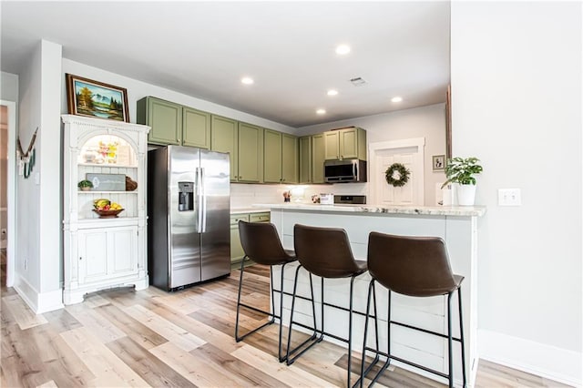 kitchen featuring stainless steel appliances, green cabinets, a breakfast bar area, light wood-type flooring, and a peninsula