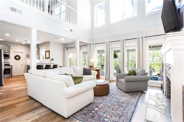 living area with healthy amount of natural light, ornate columns, light wood-style flooring, a towering ceiling, and recessed lighting