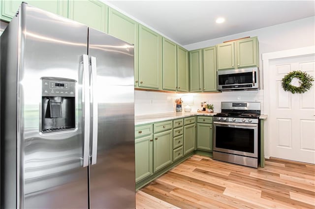 kitchen with appliances with stainless steel finishes, green cabinets, tasteful backsplash, light countertops, and light wood-style floors