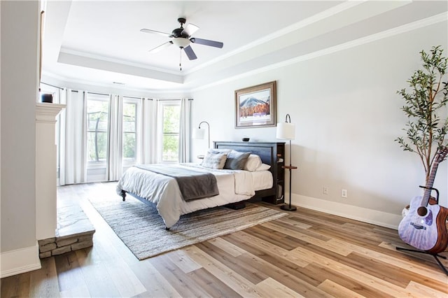 bedroom featuring a raised ceiling, ornamental molding, light wood finished floors, baseboards, and a ceiling fan