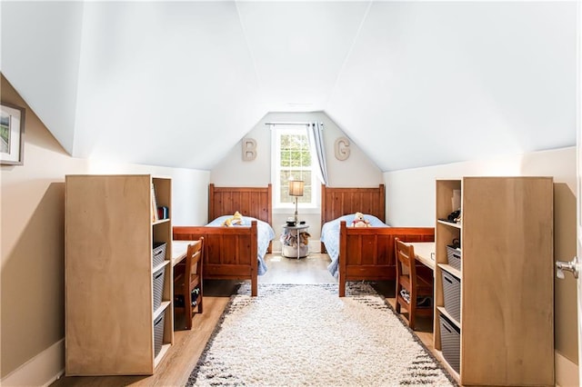 bedroom featuring light wood-style flooring, wainscoting, and vaulted ceiling