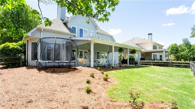 back of property with a trampoline, a chimney, and a shingled roof