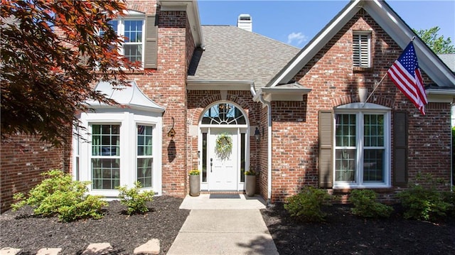 doorway to property featuring brick siding, roof with shingles, and a chimney