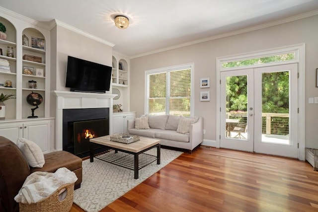 living area with wood finished floors, a lit fireplace, ornamental molding, french doors, and built in features