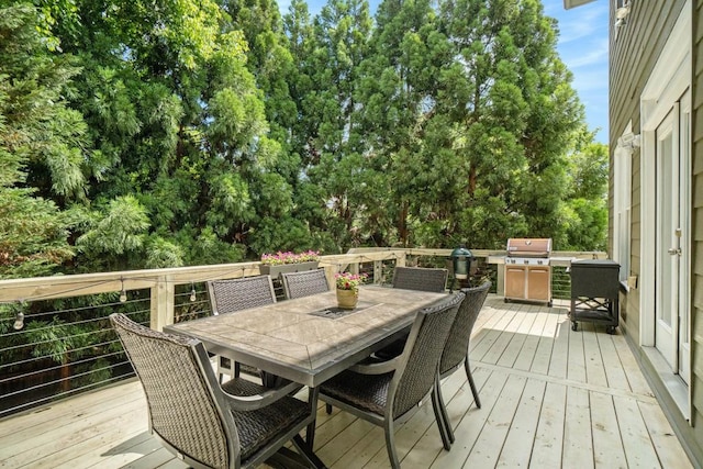 wooden terrace with outdoor dining space, grilling area, and view of wooded area