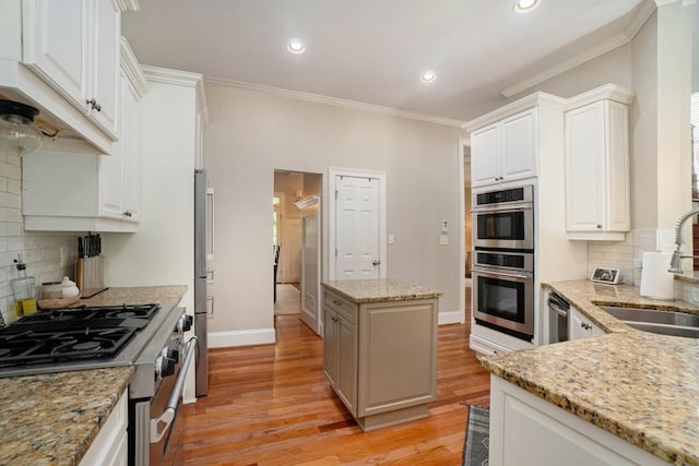 kitchen with stainless steel appliances, a sink, ornamental molding, light wood-style floors, and backsplash