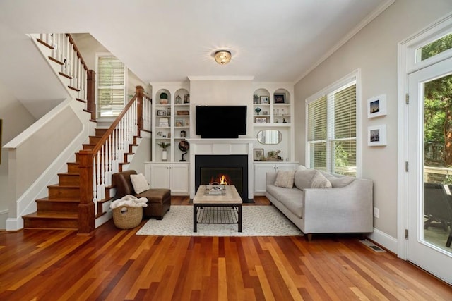 living room featuring wood finished floors, stairway, a fireplace with flush hearth, built in shelves, and baseboards