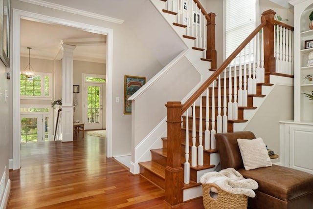 stairway with wood finished floors, ornamental molding, and decorative columns