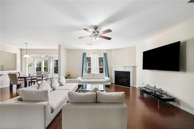 living room with ceiling fan, dark wood finished floors, a fireplace with flush hearth, and baseboards