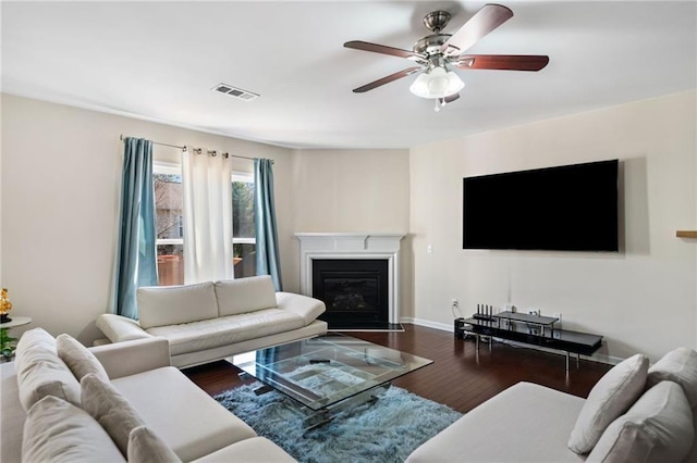living area with wood finished floors, ceiling fan, a fireplace with flush hearth, and baseboards