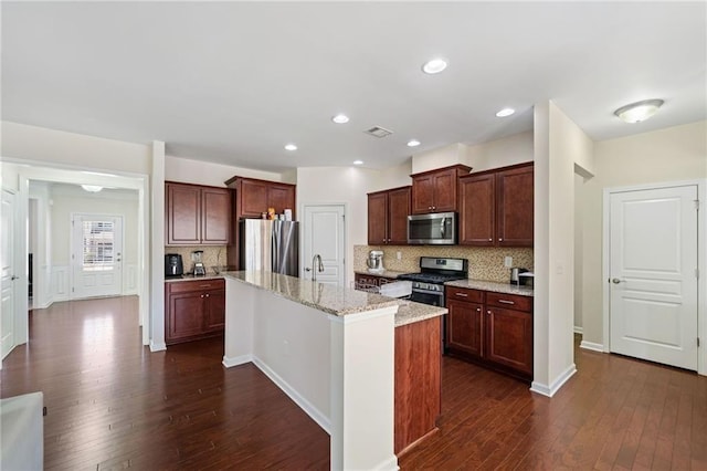 kitchen with stainless steel appliances, dark wood-style flooring, backsplash, light stone countertops, and a center island with sink