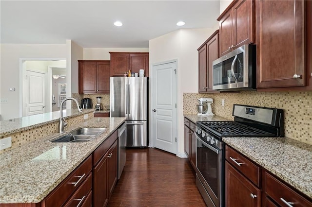kitchen with appliances with stainless steel finishes, a sink, dark wood-style flooring, decorative backsplash, and light stone countertops