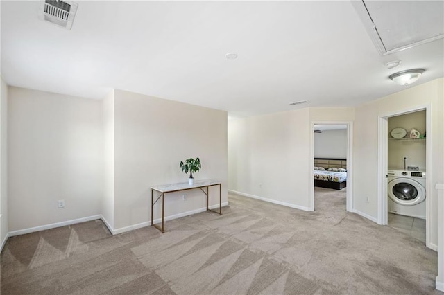 carpeted empty room with washer / dryer, attic access, and baseboards