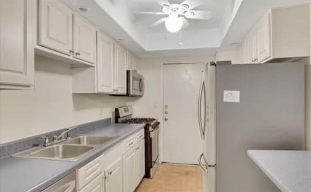 kitchen featuring ceiling fan, sink, a raised ceiling, white cabinets, and appliances with stainless steel finishes