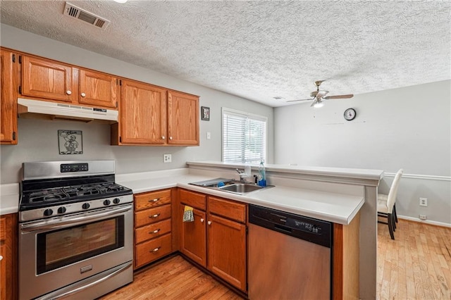 kitchen featuring stainless steel appliances, under cabinet range hood, a peninsula, a sink, and light wood finished floors