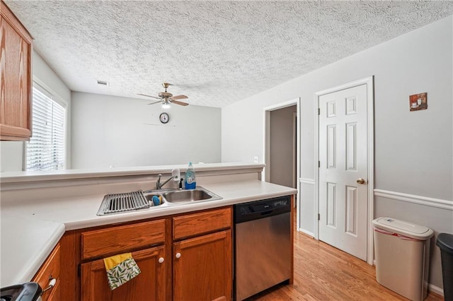 kitchen featuring stainless steel dishwasher, a sink, light wood finished floors, a ceiling fan, and light countertops