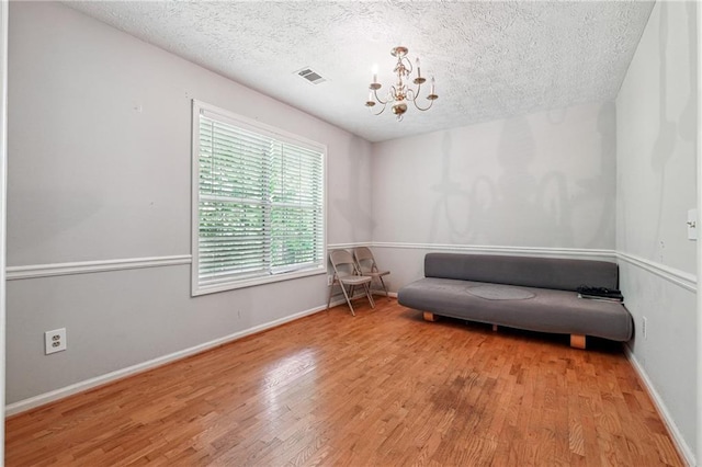 sitting room featuring a chandelier, a textured ceiling, wood finished floors, and baseboards