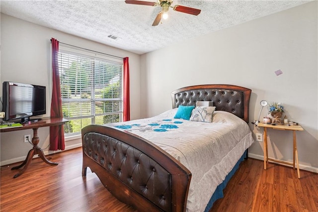 bedroom featuring multiple windows, a textured ceiling, wood finished floors, baseboards, and ceiling fan