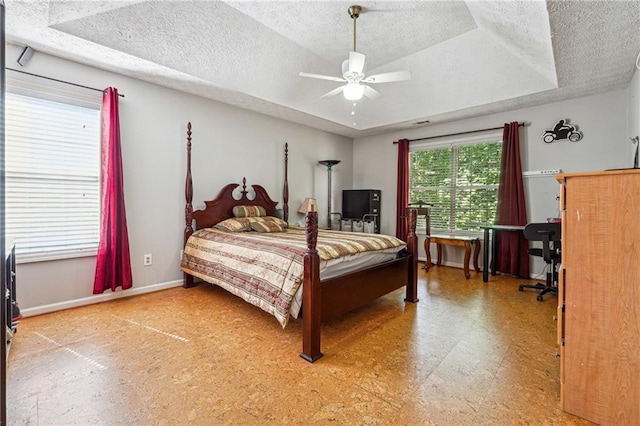 bedroom featuring a tray ceiling, a textured ceiling, tile patterned floors, baseboards, and ceiling fan