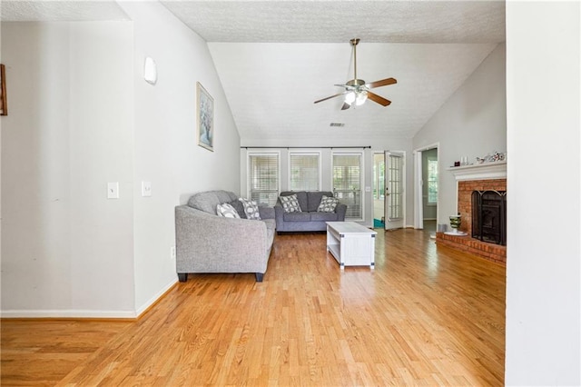 living area featuring a ceiling fan, light wood-style flooring, vaulted ceiling, baseboards, and a brick fireplace