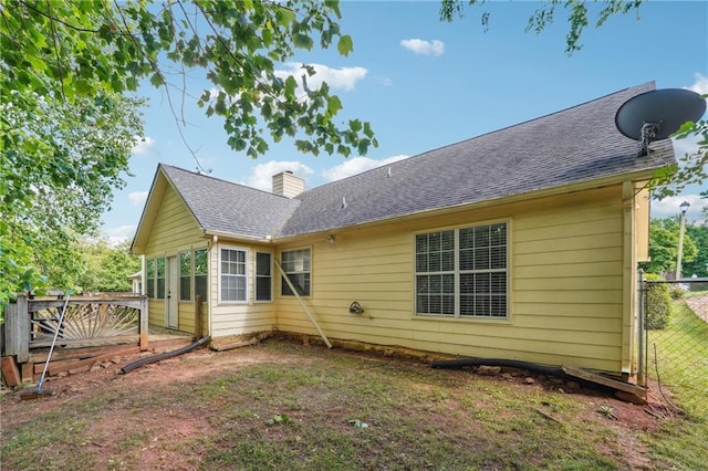back of house with fence, a chimney, and a shingled roof