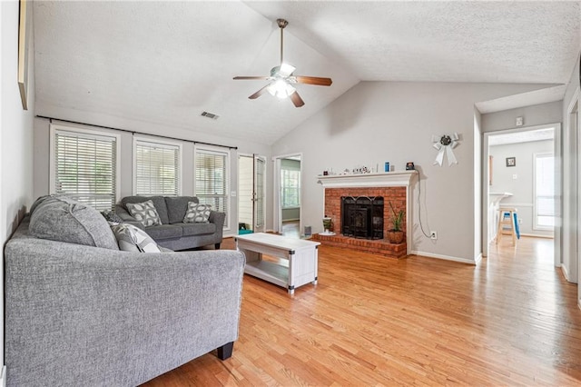 living area with ceiling fan, light wood-style flooring, lofted ceiling, healthy amount of natural light, and a fireplace